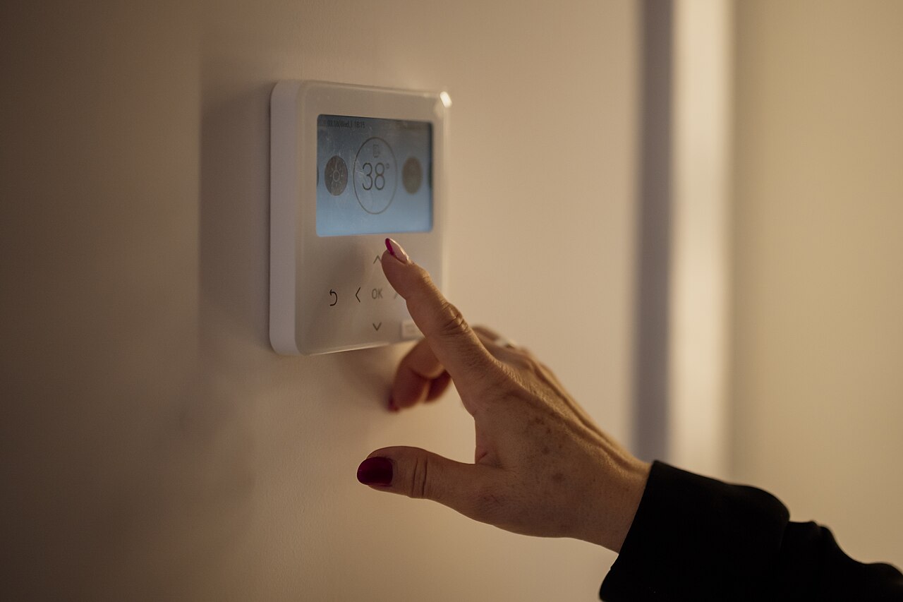 Hand adjusting the temperature on a digital wall thermostat